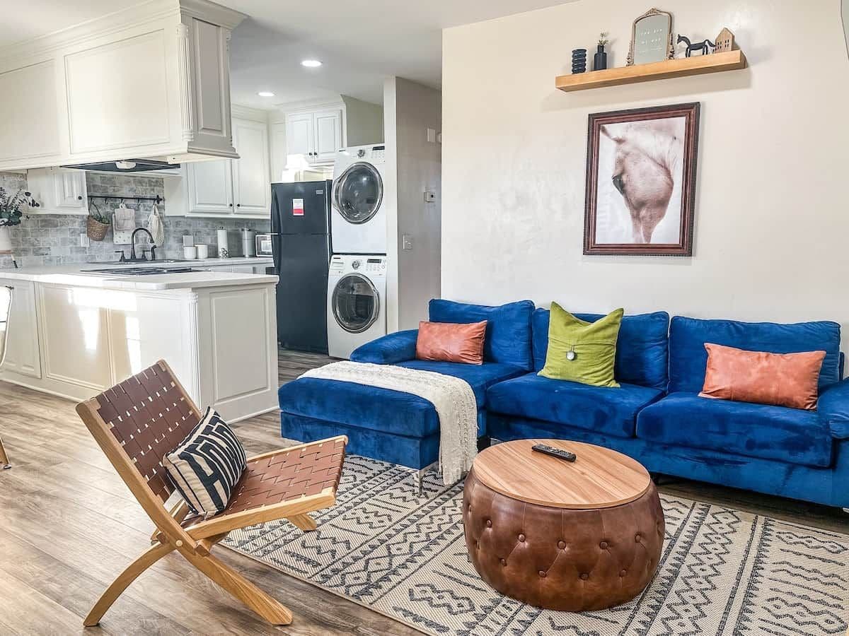 A living room with a blue sofa, a patterned rug, a wooden coffee table, and a chair with a patterned cushion.