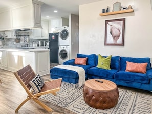 A living room with a blue sofa, a patterned rug, a wooden coffee table, and a chair with a patterned cushion.