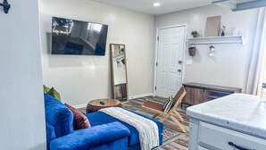 Uma sala de estar com um sofá azul, uma cadeira de madeira, uma televisão, um espelho e um armário branco.
