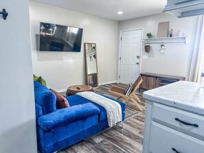A living room with a blue sofa, a wooden chair, a TV, a mirror, and a white cabinet. - ModWest Escape | Pets Welcome | Near I-40 & Rt 66 (Weatherford)