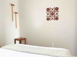 A bedroom with a bed, a small wooden table, and a wall-mounted game board.