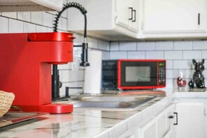 A kitchen with a red appliance, a microwave, and white cabinets.