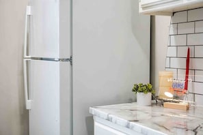Une cuisine avec un réfrigérateur blanc, un plan de travail en marbre et une petite plante en pot.