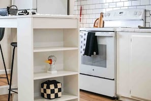 Une cuisine avec des meubles blancs, une cuisinière blanche et un sac à carreaux posé sur une étagère.