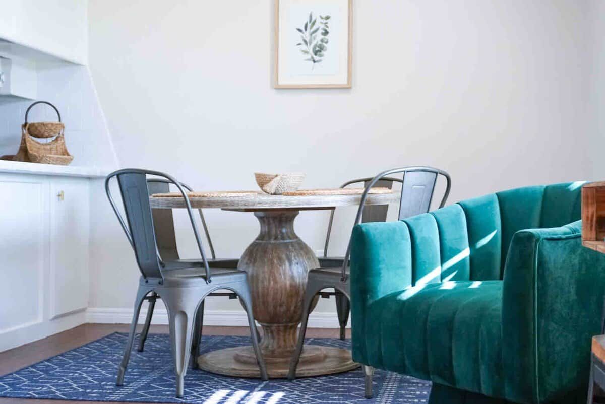 Un coin repas avec une table ronde, quatre chaises, un canapé de couleur turquoise et une estampe botanique encadrée accrochée au mur.