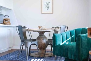 Un coin repas avec une table ronde, quatre chaises, un canapé de couleur turquoise et une estampe botanique encadrée accrochée au mur.