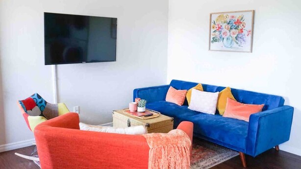 A living room with a blue sofa, a red armchair, a flat-screen TV, and a framed floral artwork on the wall. - Colorful Retreat | Near I-40 &SWOSU | Pets Welcome (Weatherford)