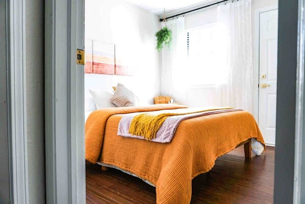 A bedroom with a bed, a window with curtains, a plant, and a door.