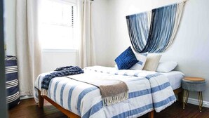 A bed with striped bedding, a bedside table, a window with curtains, and a hammock. - Colorful Retreat | Near I-40 &SWOSU | Pets Welcome (Weatherford)