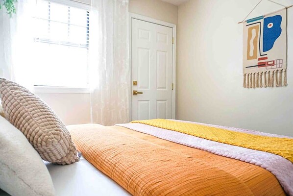 A bedroom with a bed, pillows, a window with blinds, and a wall-mounted artwork.