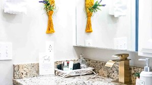 A bathroom with a granite countertop, a gold faucet, and yellow macramé wall hangings. - Colorful Retreat | Near I-40 &SWOSU | Pets Welcome (Weatherford)