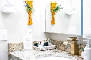 Une salle de bain avec un comptoir en granit, un robinet doré et des décorations murales en macramé jaune.