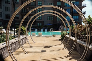Un espace piscine agrémenté d’une sculpture circulaire en métal, de chaises longues et d’un bâtiment en arrière-plan.