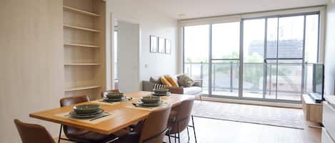 A dining area with a wooden table set for six, surrounded by chairs, and a sofa with cushions in the background.