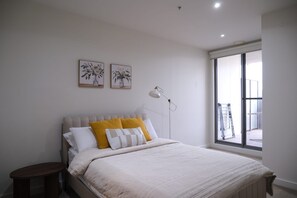 Un dormitorio con cama, mesita de noche, lámpara y ventana con vistas al exterior.