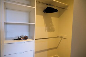 A walk-in closet with open shelves, a hanging rack, and a pair of scissors on the bottom shelf. - Stylish St Kilda Apartment | 2BR, 2 Bathrooms, Balcony + Secure Parking (St Kilda)