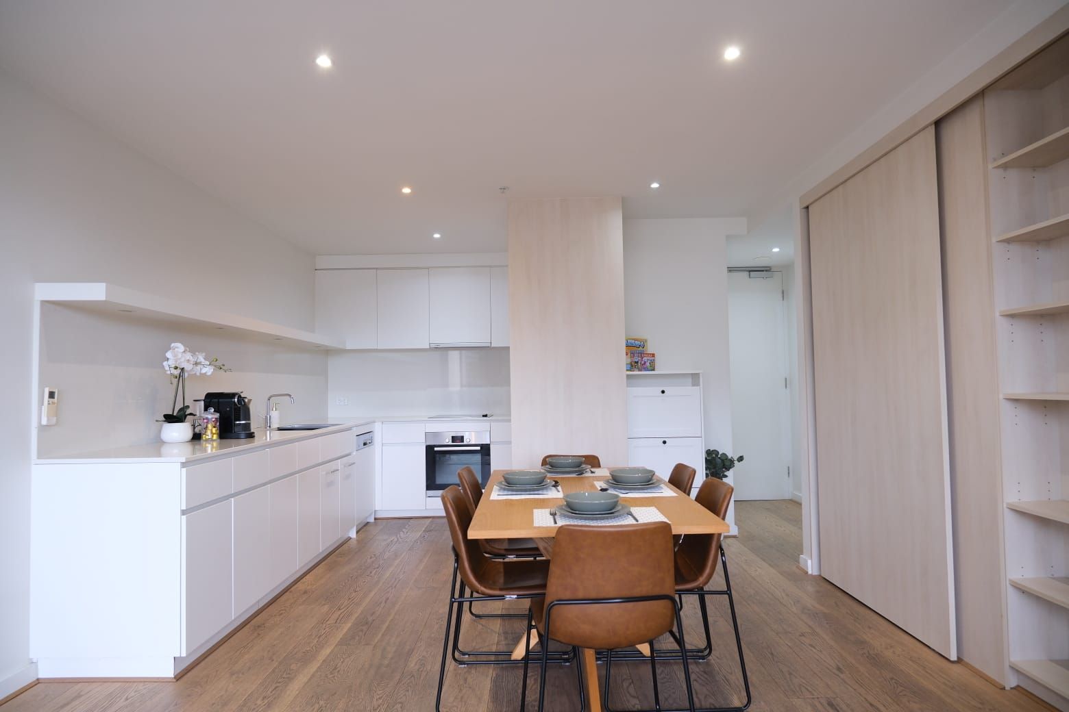 Een moderne keuken met witte kasten, een eettafel voor zes personen en een houten vloer.