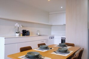 Una cocina moderna con armarios blancos, una mesa de comedor con cuencos y platos, y una cafetera sobre la encimera.