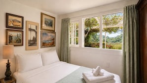 Habitación de hotel con cama, mesita de noche, lámpara y ventana con cortinas.