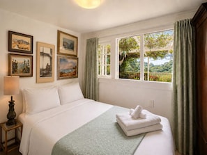 Quarto de hotel com cama, mesa de cabeceira, luminária e janela com cortinas.
