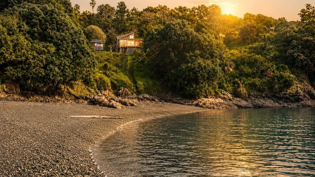 Una propiedad frente a la playa con una casa rodeada de vegetación densa y una playa de guijarros.