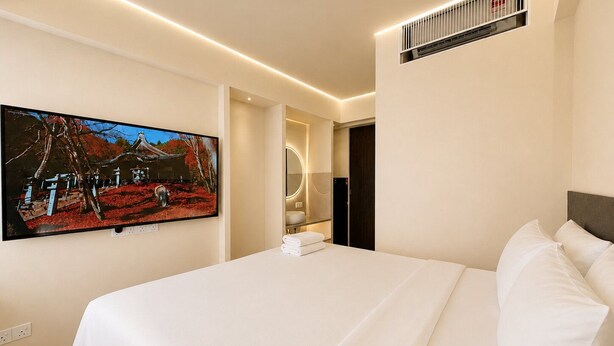 A hotel room with a bed, a television mounted on the wall, and a bathroom with a mirror and sink. - Central Georgetown Homestay for 8 Pax . Chulia Street, Penang (George Town)
