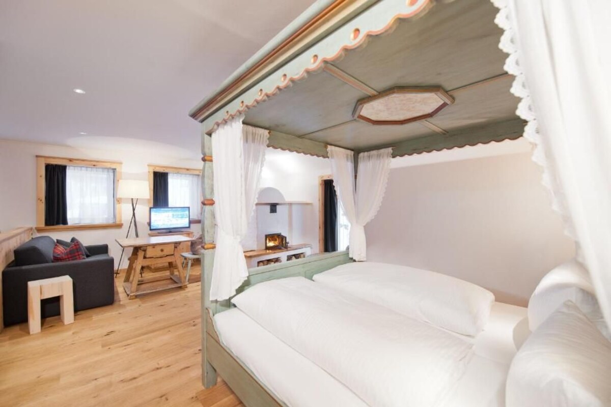 Une chambre à coucher avec un lit à baldaquin, un bureau avec un ordinateur, un canapé et une fenêtre avec des rideaux.