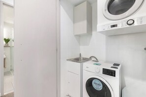 Ein moderner Waschraum mit einer Frontlader-Waschmaschine und einem Trockner, einem kleinen Waschbecken und einem Schrank über dem Trockner.