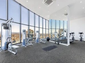 A gym with exercise equipment, large windows, and a city view. - OceanDreams Lvl 46 2BR Skyhome | 2 Pools & Gym (Surfers Paradise)