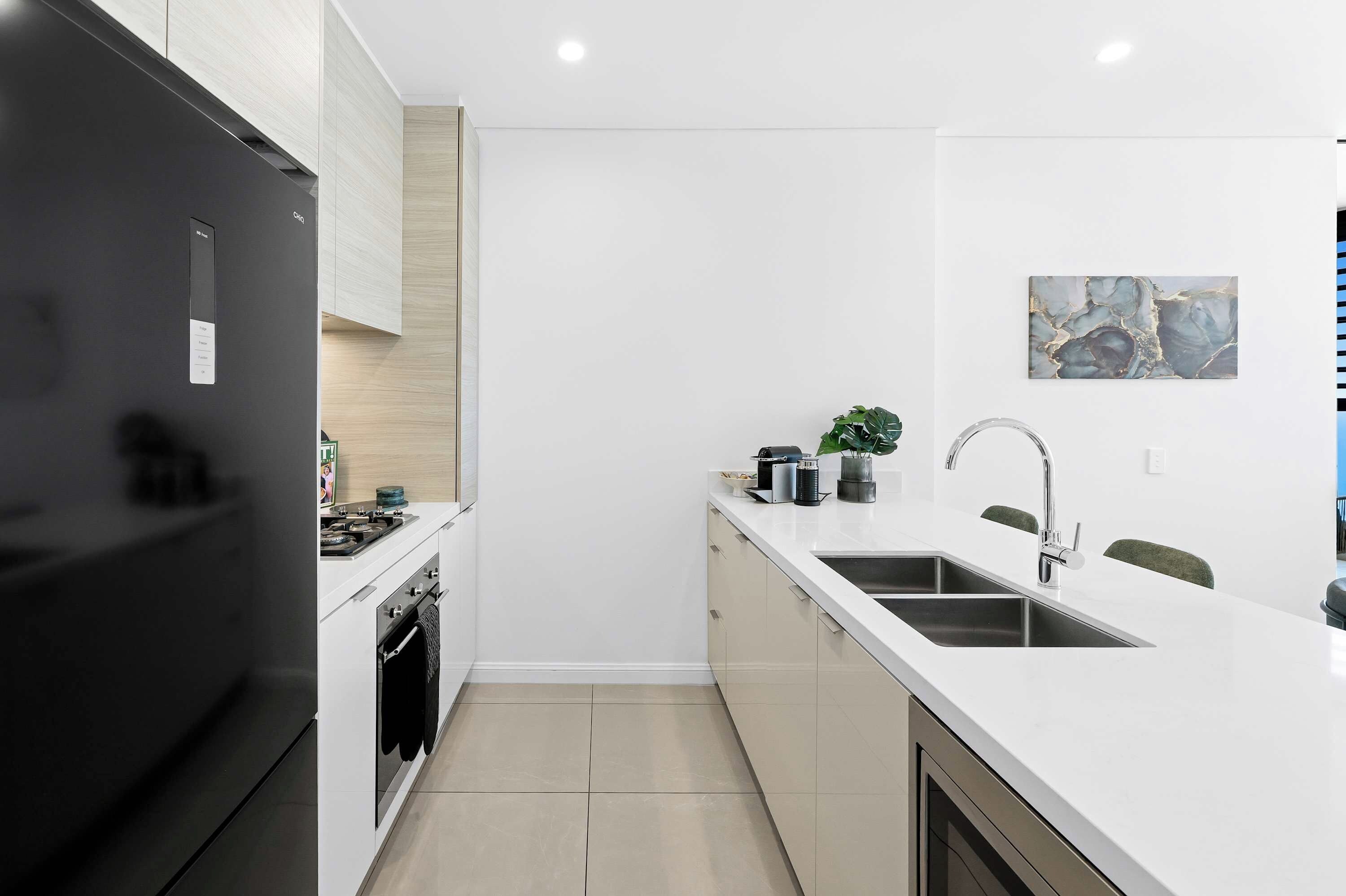 Una cocina moderna con refrigerador negro, muebles blancos, pileta de acero inoxidable y salpicadero de mármol.