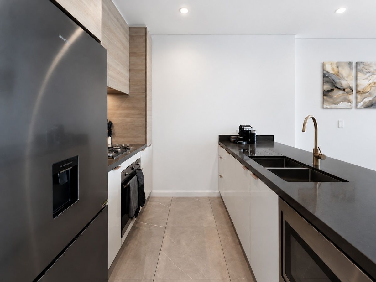 A modern kitchen with a stainless steel refrigerator, a built-in oven, and a black countertop.