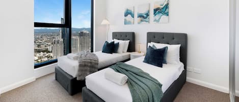 A modern hotel room with a city view, two beds, a large window, and artwork on the wall.