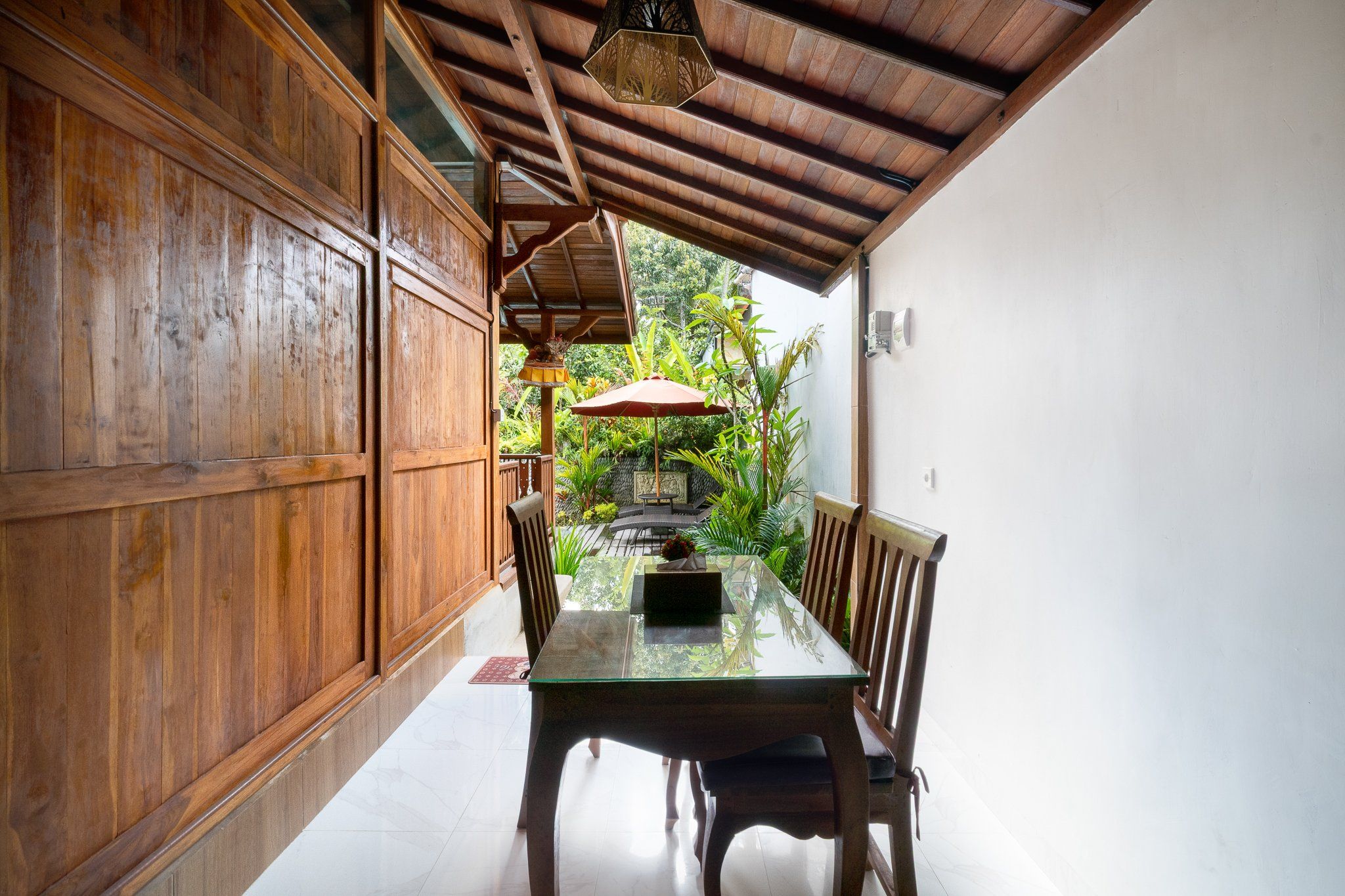 Un interior de madera con una mesa y sillas de vidrio, un candelabro y vistas al exterior con follaje.