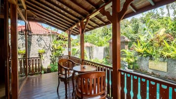 A wooden deck with a table and chairs, surrounded by a stone wall and lush greenery.