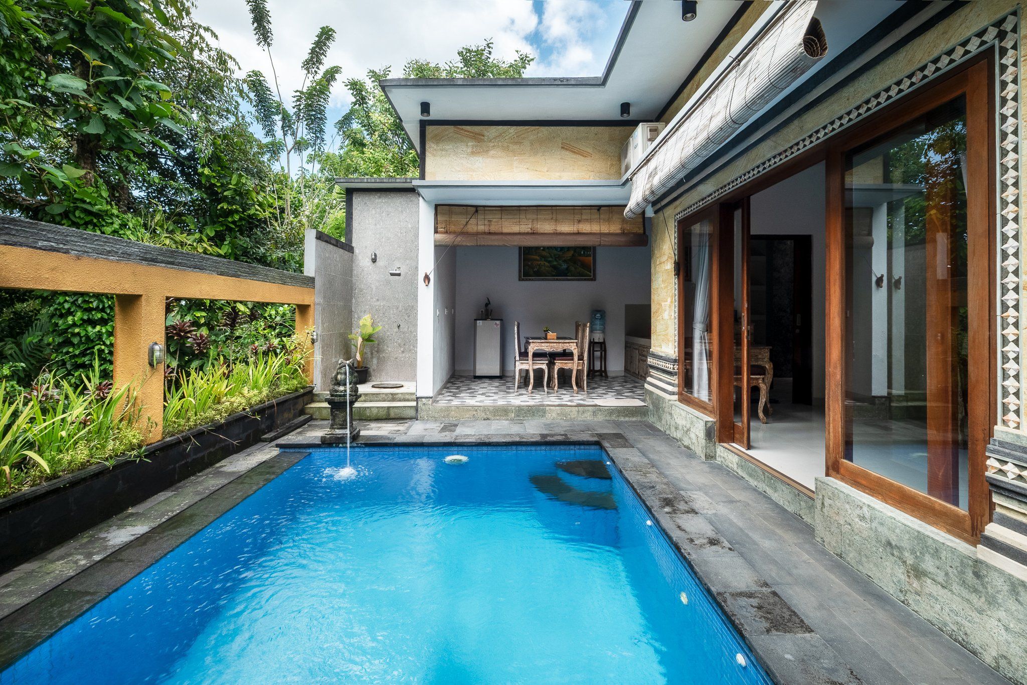 Une piscine avec une terrasse en bois, un coin repas avec des chaises et une vue sur la verdure environnante.