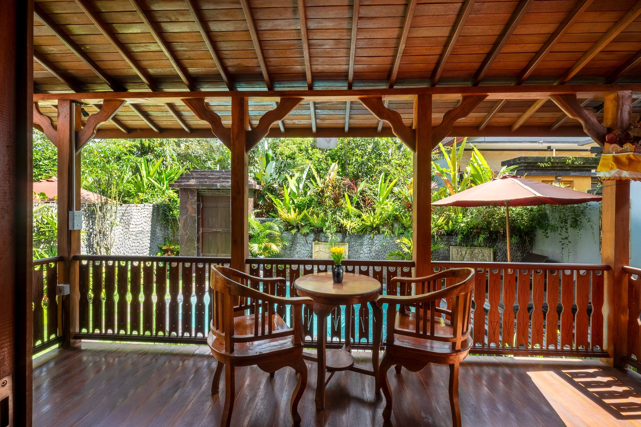 A wooden deck with a table and chairs, surrounded by a wooden railing and lush greenery.