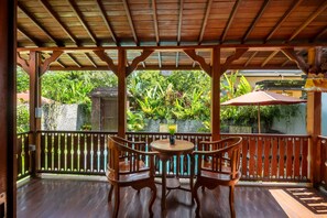 A wooden deck with a table and chairs, surrounded by a wooden railing and lush greenery.