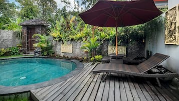 Ein Schwimmbecken mit Holzterrasse, Liegestühlen und Sonnenschirm.