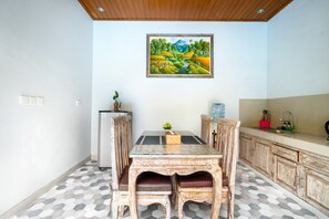 A dining area with a wooden table and chairs, a painting above, and a kitchen area with cabinets and a sink.