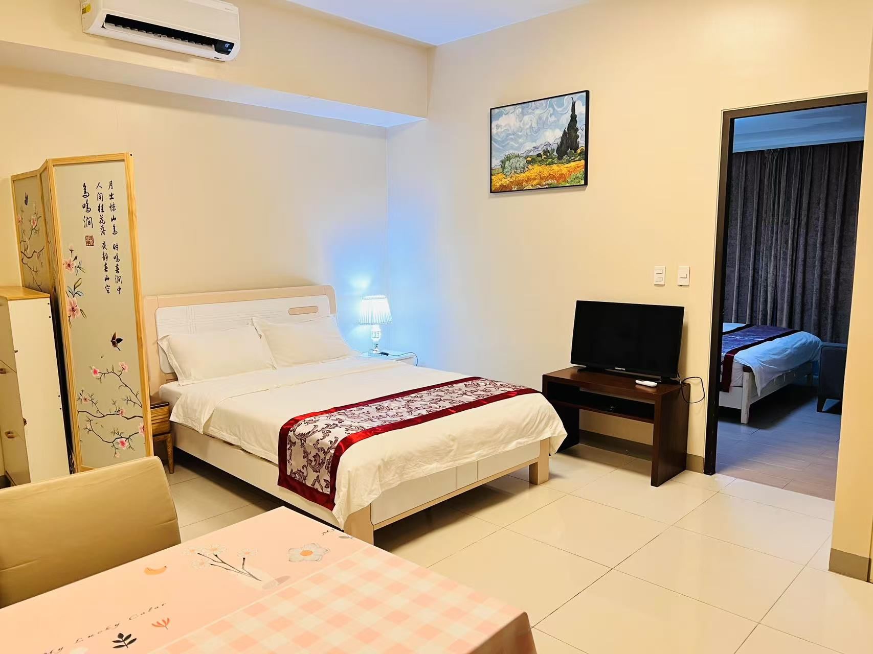 Habitación de hotel con cama, mesita de noche con lámpara, televisión, escritorio con silla y un cuadro en la pared.
