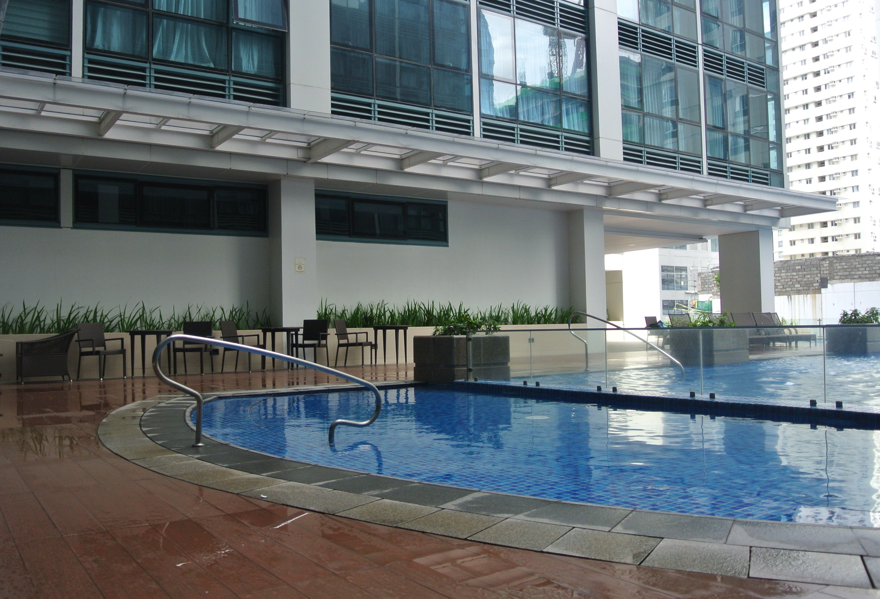 An indoor swimming pool with a tiled floor, surrounded by lounge chairs and a glass railing.