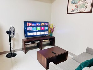 Ein Wohnzimmer mit Flachbildfernseher, einem Standventilator, einem Couchtisch und einer Couch.