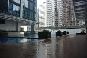 A wet outdoor area with a pool, seating, and high-rise buildings in the background. - One Uptown Residence BGC Work & Unwind | Heart of BGC (Makati City)