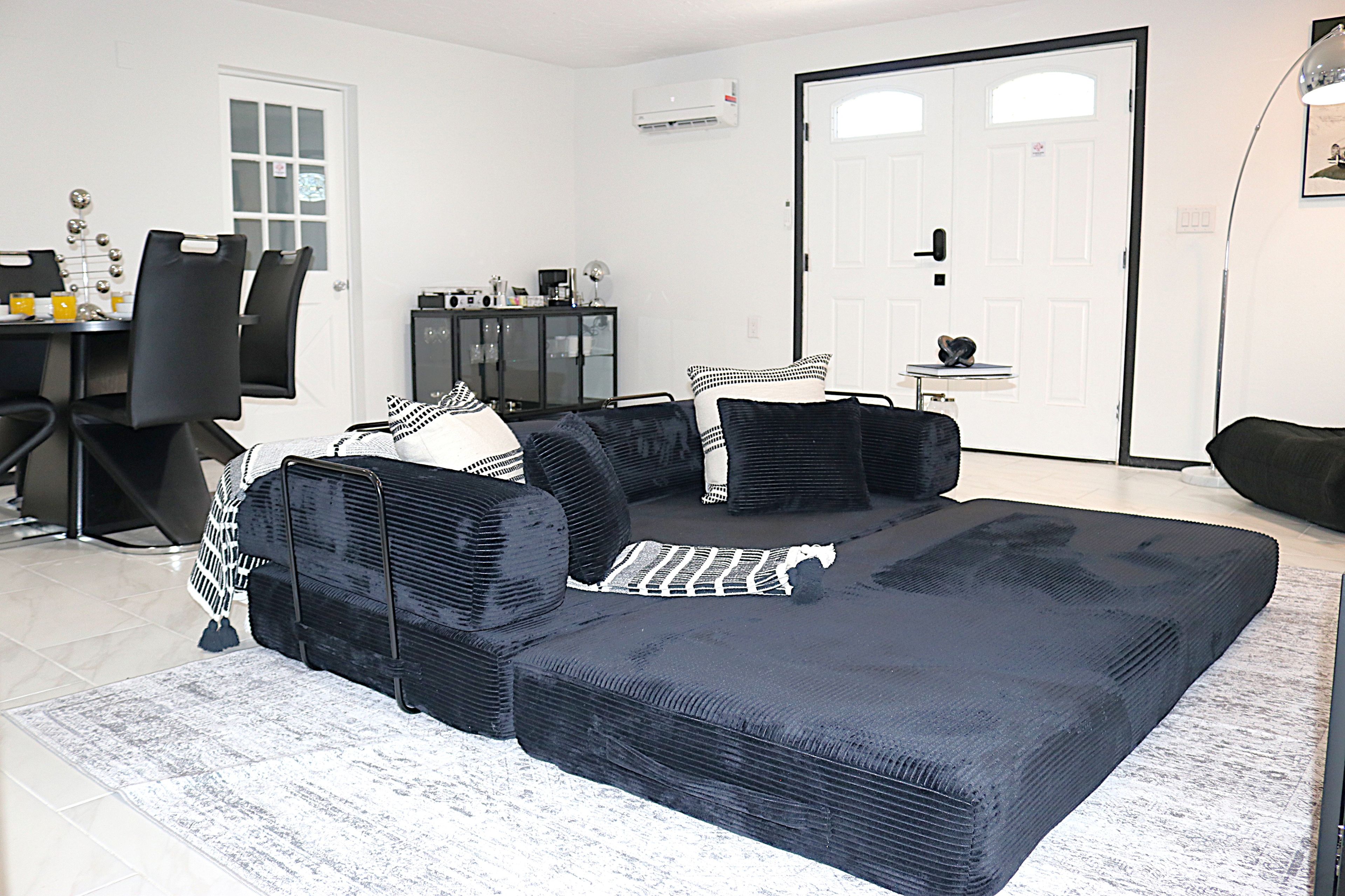 A living room with a sectional sofa, a dining table with chairs, a cabinet, and a door.