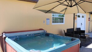 A hot tub with a beige canopy overhead, a window with a view, and a door with a fire extinguisher mounted on the wall. - Harmony Luxe at Sarasota (Sarasota)
