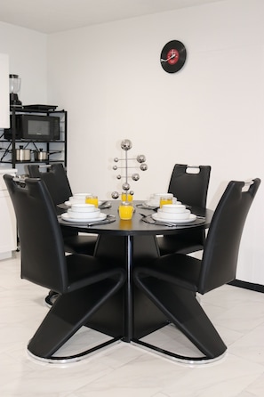 Un coin repas avec une table ronde, des chaises noires et une horloge fixée au mur.
