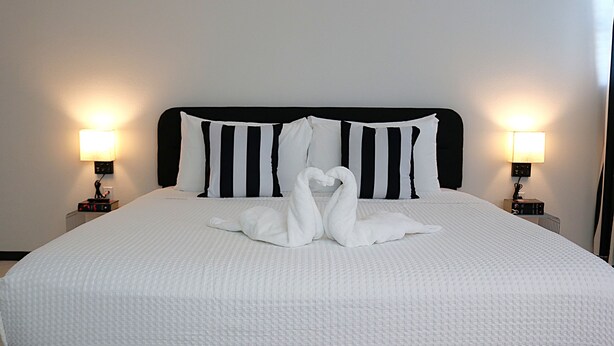 A neatly made bed with a white bedspread and black and white striped pillows, flanked by two bedside lamps. - Harmony Luxe at Sarasota (Sarasota)