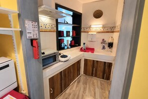 Eine kleine Küche mit eingebautem Ofen, einer Kaffeemaschine und einem roten Wasserkocher auf der Arbeitsplatte.