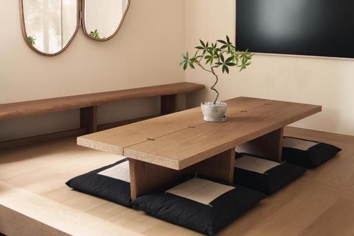 Una habitación minimalista con una mesa de madera, bancos y una planta en maceta.