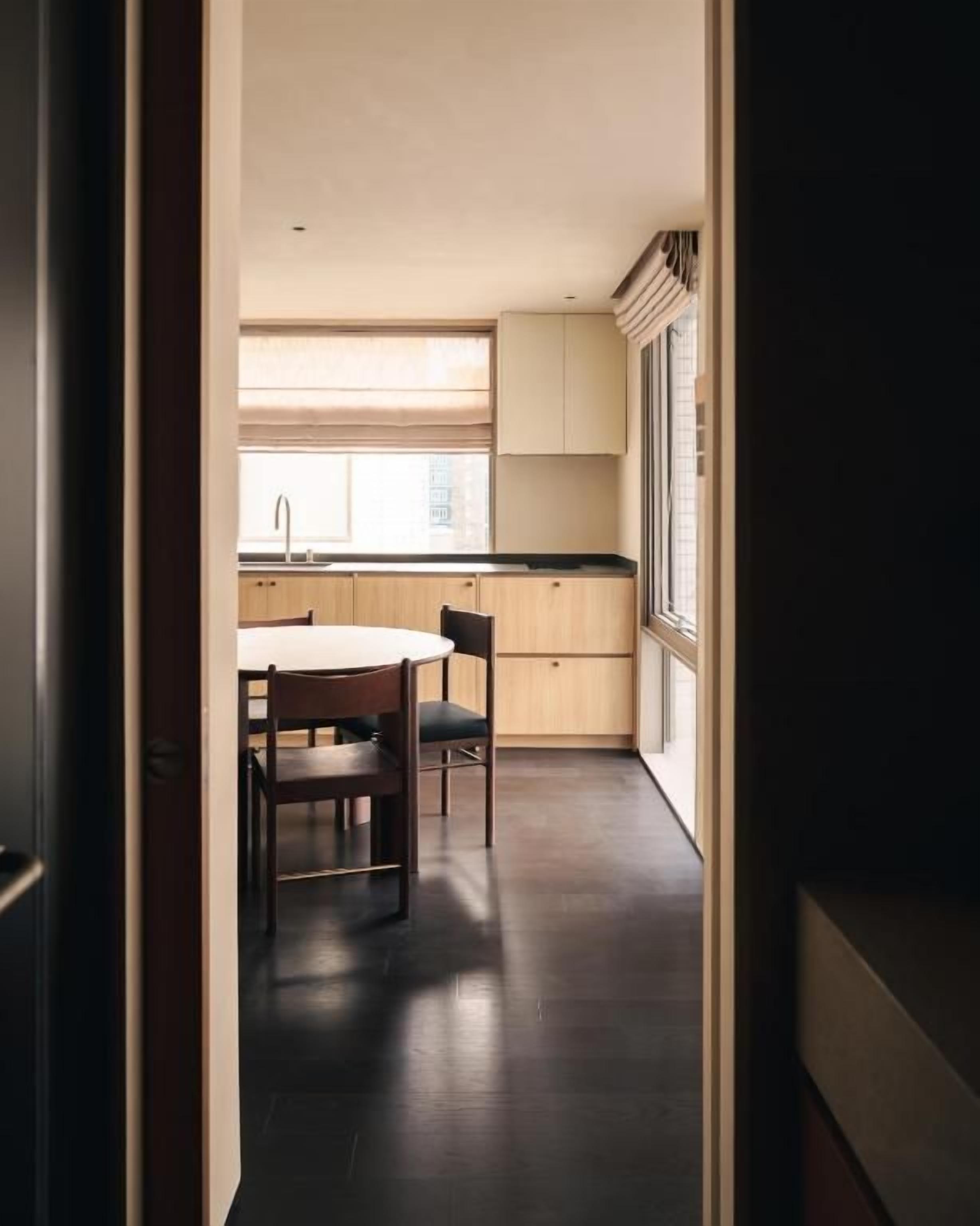 A narrow hallway leading to a kitchen with a dining table and chairs.